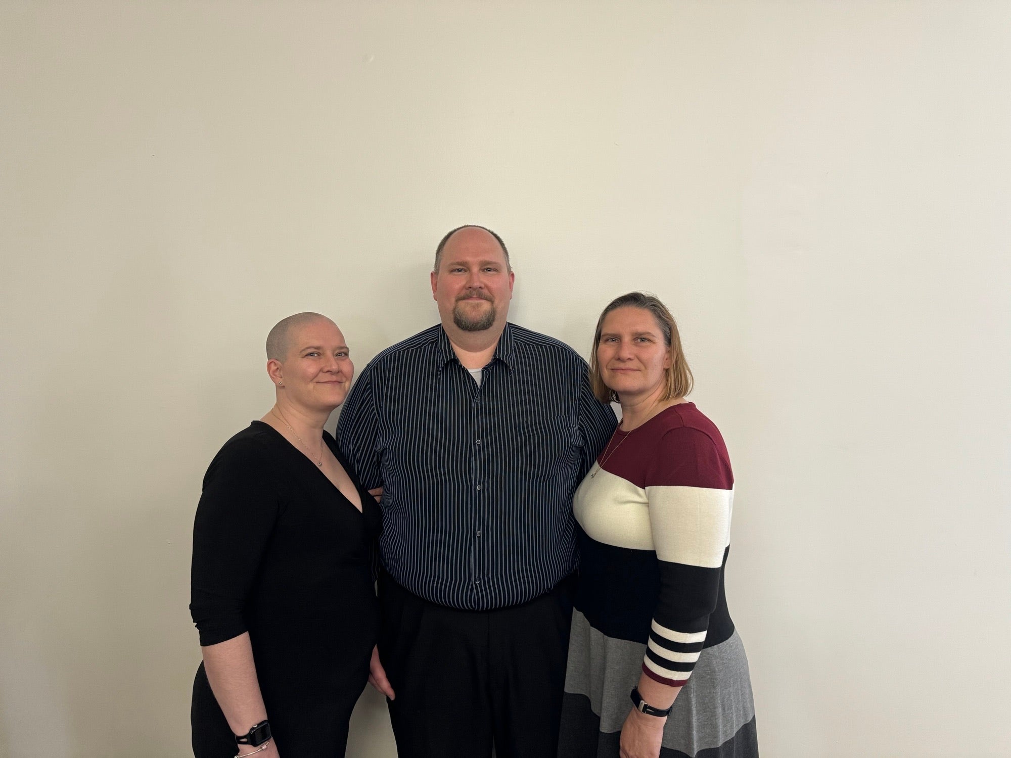 3 adults standing against wall